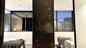 A modern hotel room with a large window, a bed, a seating area, and a decorative wall panel. - 2 BR in High-Rise Building at Manhattan (Melbourne)