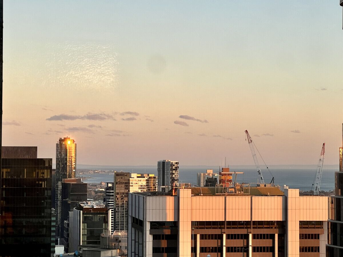 A cityscape with modern buildings, construction cranes, and a view of the sea.