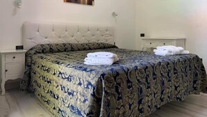 A bedroom with a tufted headboard, a floral bedspread, and a cityscape painting on the wall. - Hotel Marittima (Rimini)