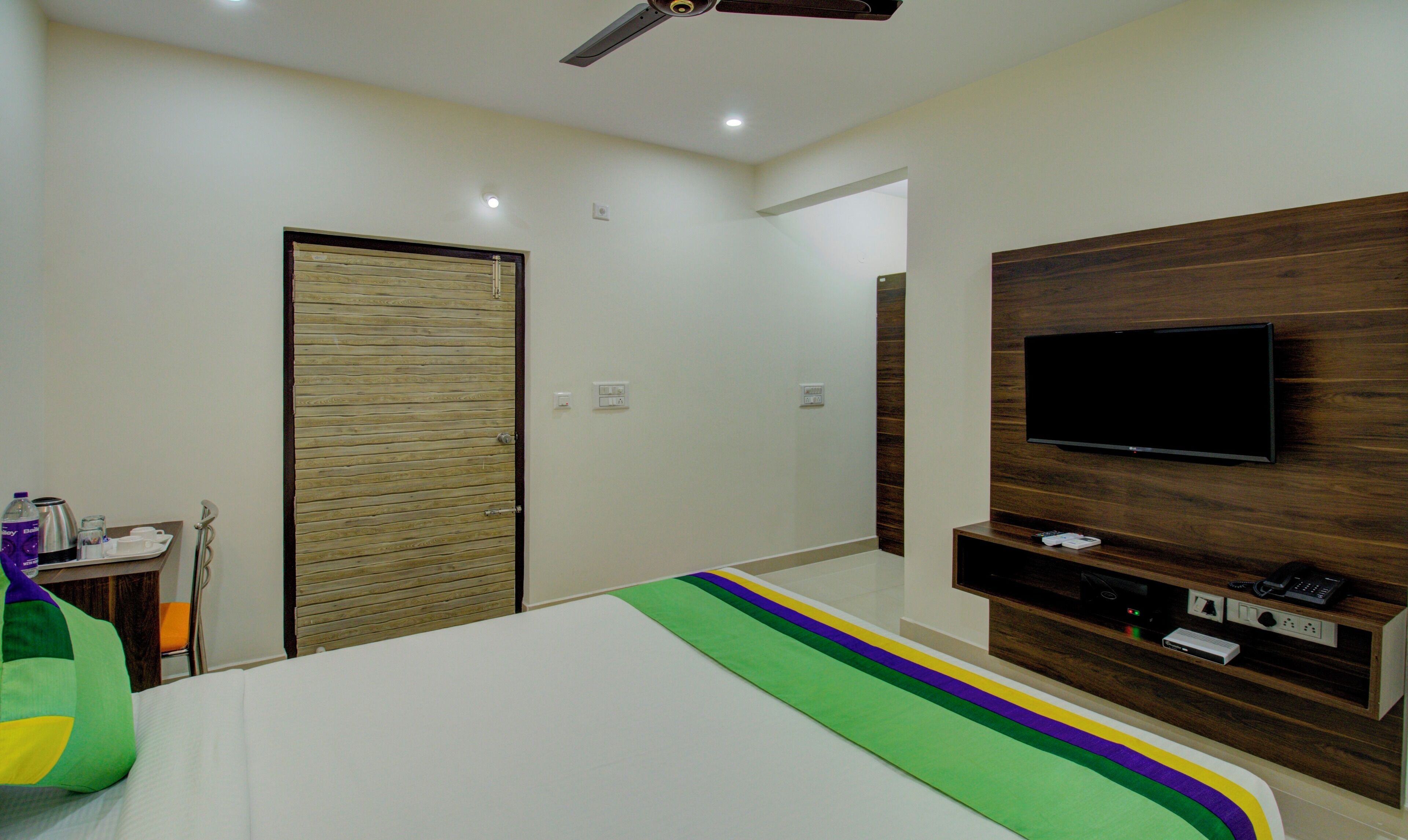Camera d'albergo con un letto, una TV a parete, una porta in legno e un tavolino con un vassoio.