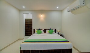 A bedroom with a bed, a nightstand, a lamp, and an air conditioning unit. - Treebo Fortune Stay Inn (Bengaluru)