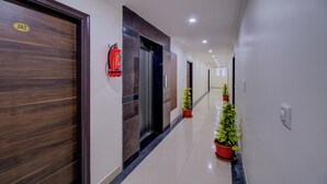 Un couloir avec une porte en bois portant le numéro 202, un extincteur et des plantes en pot le long du mur.