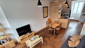 A modern living room with a sofa, wooden herringbone flooring, a TV, and a dining area with a wooden table and chairs. - Appartement Belle vue Centre Ville Fécamp 1 km de la Plage (Fécamp)