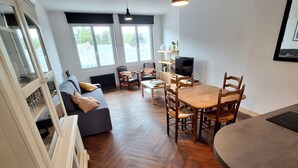 A spacious living area with a herringbone wooden floor, a dining table with chairs, a sofa, and a television. - Appartement Belle vue Centre Ville Fécamp 1 km de la Plage (Fécamp)