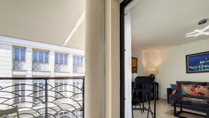 Un balcón con barandilla de metal, una silla y una mesa.