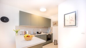 A modern kitchen with a white countertop, a sink, a stove, and a trash bin. There is a clock on the wall and a framed picture above the counter. - Billie Holiday apartment with balcony (Split)
