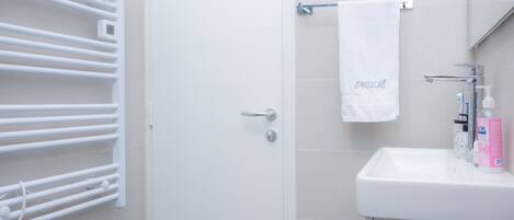 A bathroom with a white door, a towel rack, a sink with a mirror, and a bottle of hand soap.