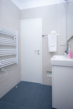 Ein Badezimmer mit einer weißen Tür, einem Handtuchhalter, einem Waschbecken mit Spiegel und einer Handseifenflasche.