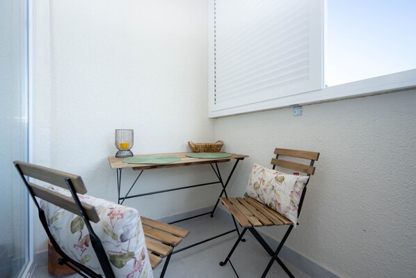 Ein kleiner Balkon mit einem Holztisch, zwei Stühlen, einem Korb und einer Lampe.