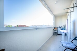 Ein Balkon mit Blick auf Gebäude, ein Stuhl und ein kleiner Tisch mit Bügelbrett.