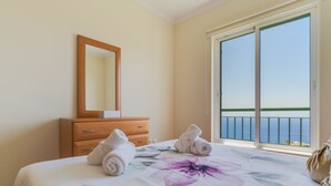 Une chambre d’hôtel avec un lit, une commode en bois, un miroir et un balcon donnant sur la mer.