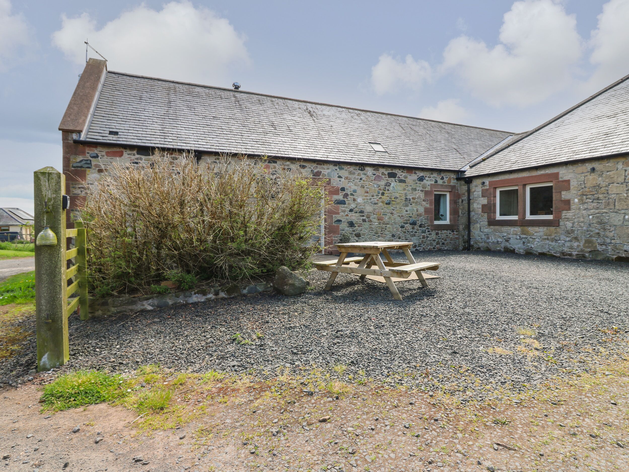 A stone building with a gravel driveway and a picnic table.
