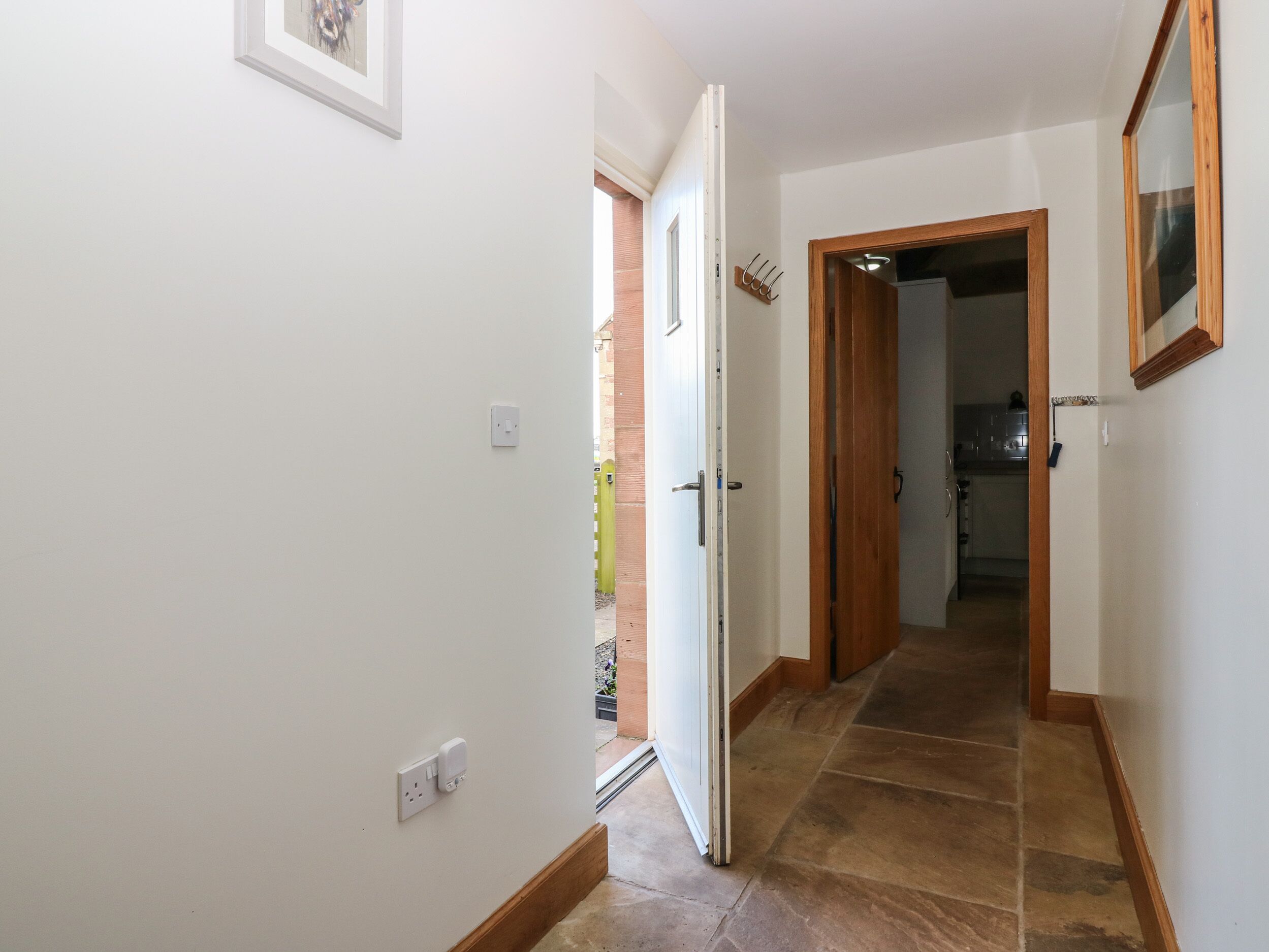 A hallway with a white wall, a wooden door, and a tiled floor.