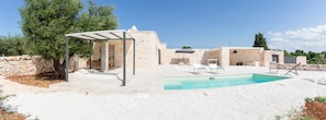 Eine Steinvilla mit Swimmingpool, Sitzgelegenheiten im Freien und einer Pergola.