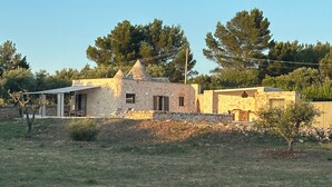 Un edificio de piedra con techo cónico, rodeado de un campo cubierto de hierba y árboles.