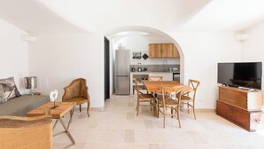 Una sala de estar moderna con un sofá, una mesa de comedor de madera y sillas, que da a una cocina con un refrigerador y armarios.