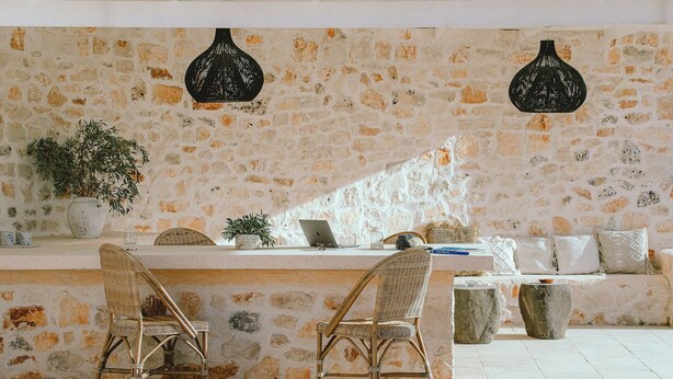 Una habitación con paredes de piedra, sillas de mimbre, una mesa y lámparas colgantes.