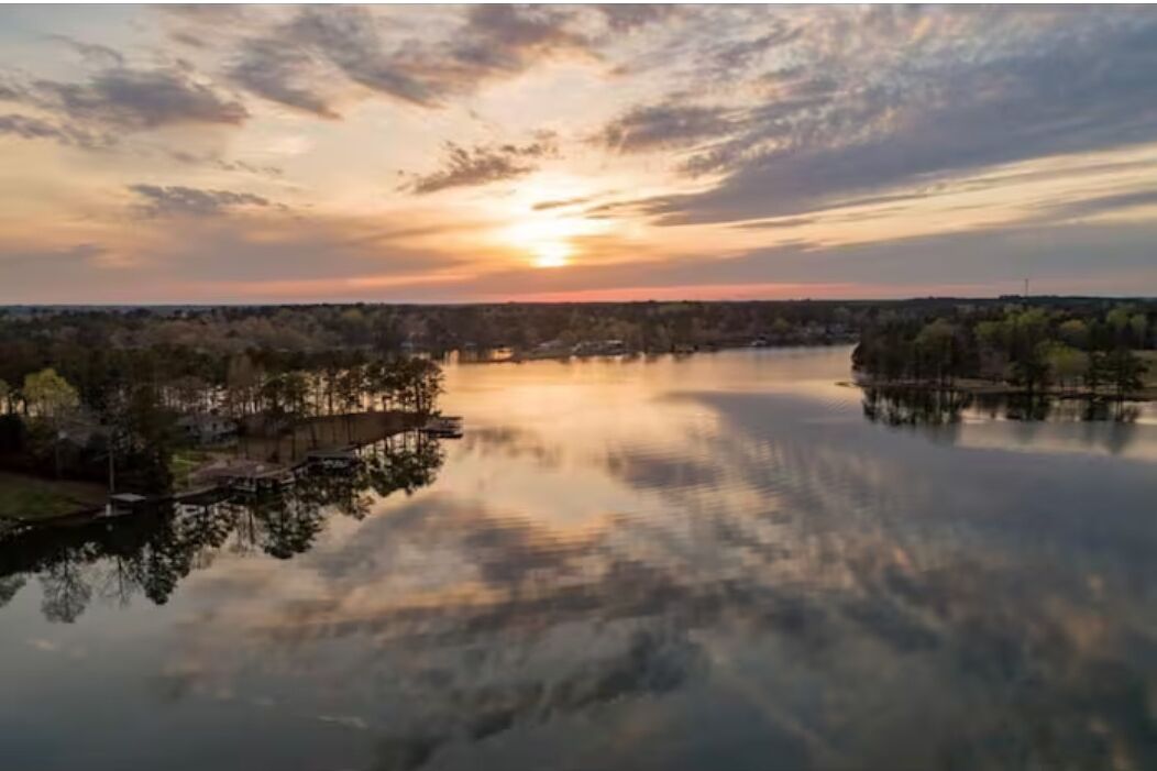 A serene lakeside view with a sunset, calm water, and a dock extending into the lake.