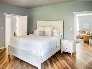 Une chambre à coucher avec un grand lit, une table de chevet et une commode. Une porte donne accès à une autre pièce.