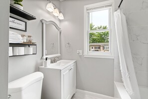 A modern bathroom with a toilet, sink, and shower. There is a window with a view of a house outside. - Stylish, Relaxing & Comfy 3 BDR Home. 2 minutes to Lake Compounce (Bristol)