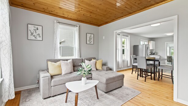 A modern living room with a grey sofa, white coffee table, and a dining area with a wooden table and chairs.