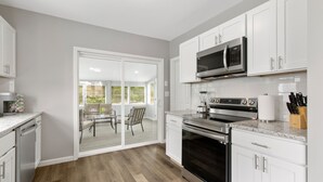 A modern kitchen with white cabinets, stainless steel appliances, and a sliding glass door leading to a patio with outdoor seating.