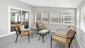 A modern interior with a grey floor, two beige chairs, a small table with a plant, and large windows with blinds.