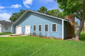 A single-story house with a blue exterior, a brick chimney, and a front yard with grass and small plants. - KING BEDS! Spacious, Central, Quiet (Daytona Beach)