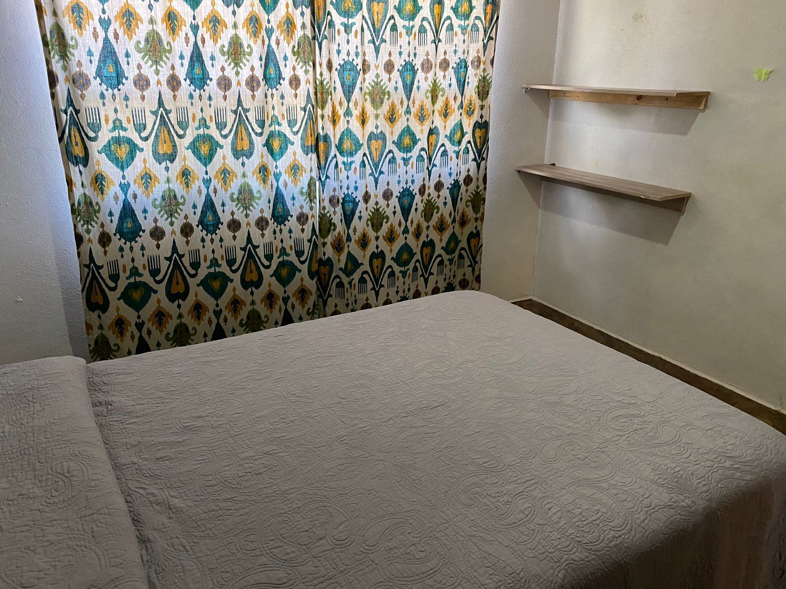 Een kamer met een bed, gordijnen met een patroon en twee houten planken aan de muur.