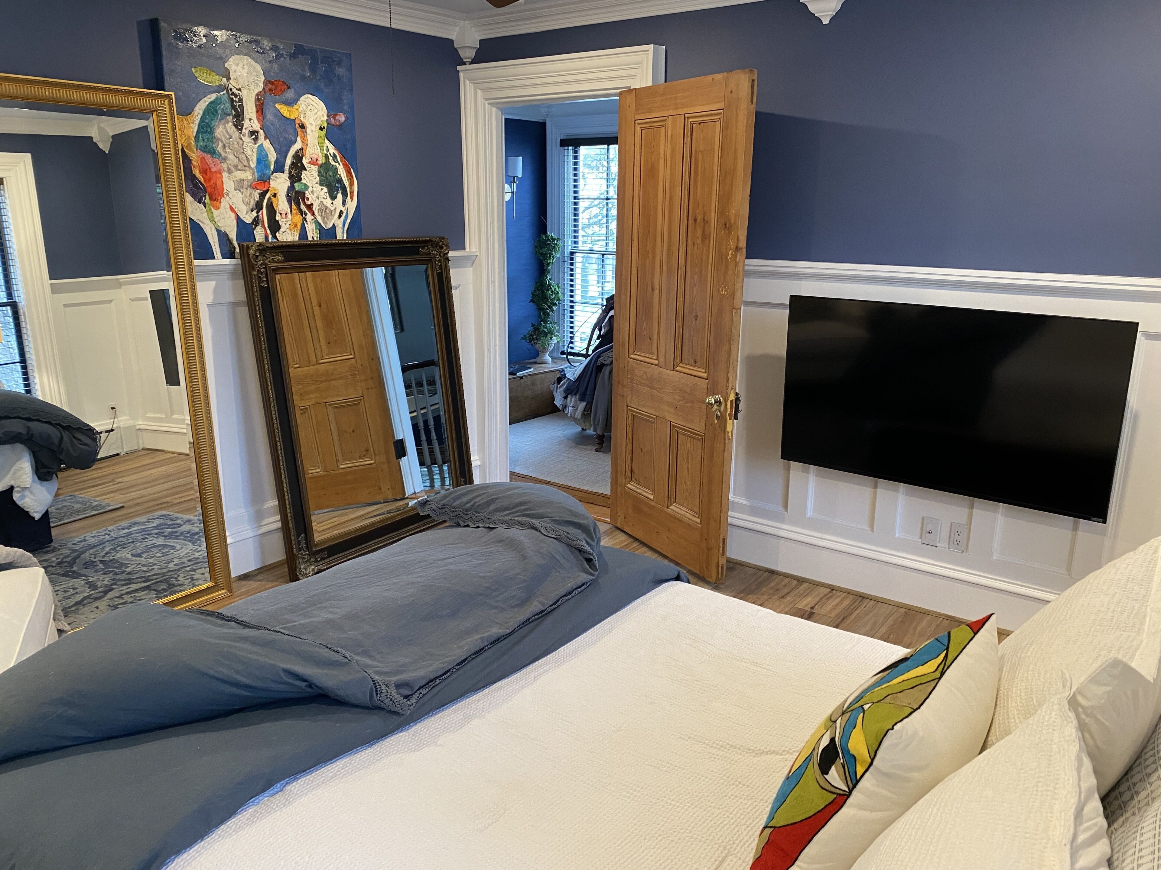 Un dormitorio con cama, televisor montado en la pared, puerta de madera y espejo.
