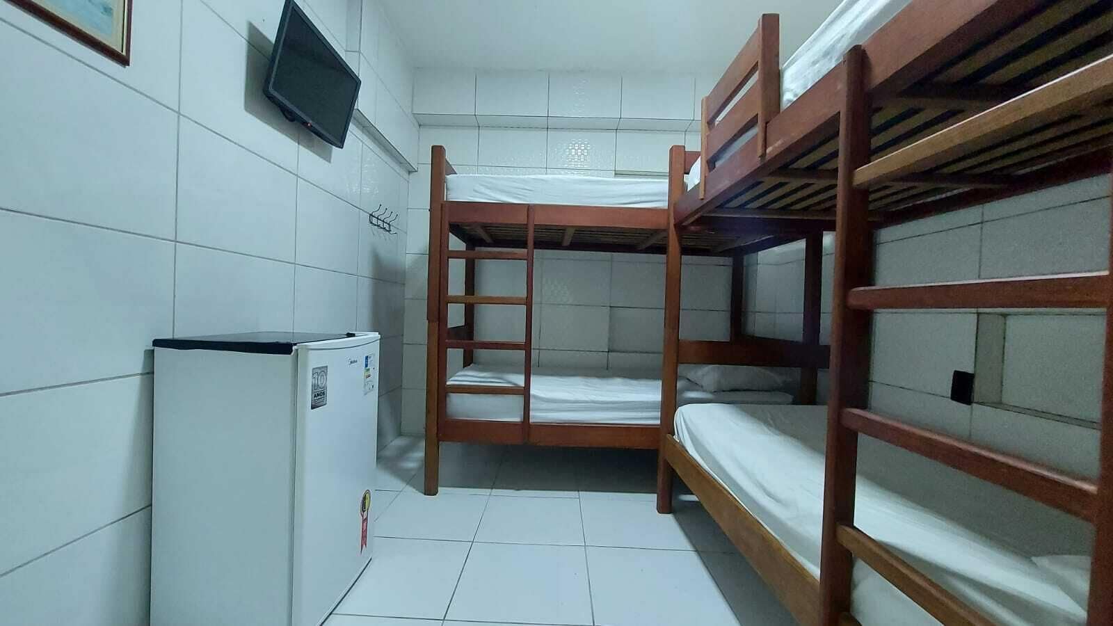 Ein Schlafraum mit Etagenbetten, einem kleinen Kühlschrank und einem an der Wand montierten Fernseher.
