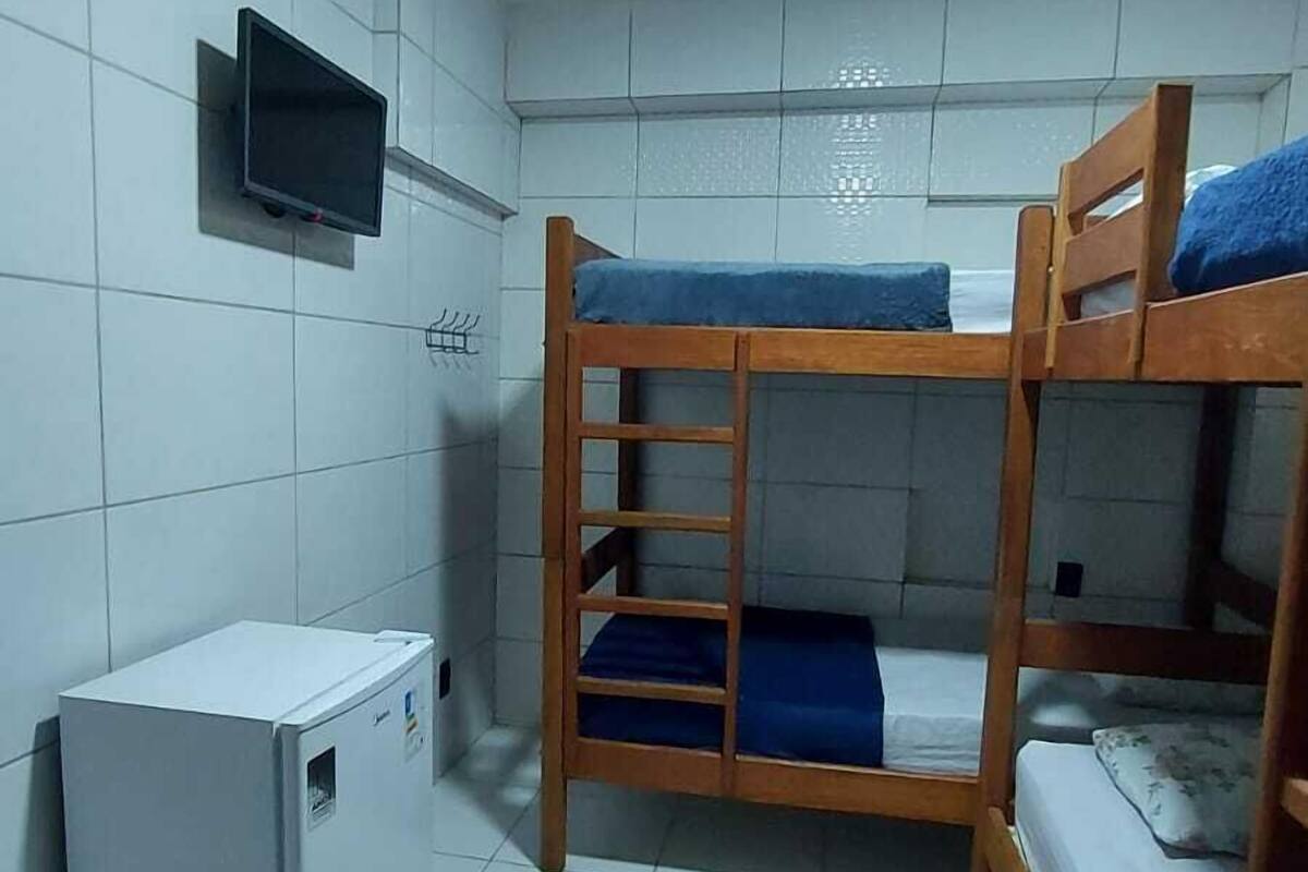 A dormitory room with bunk beds, a television mounted on the wall, and a small refrigerator.