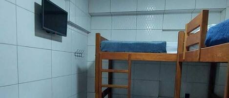 A dormitory room with bunk beds, a television mounted on the wall, and a small refrigerator.