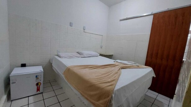 A small, clean room with a bed, a small heater, and a wooden door.