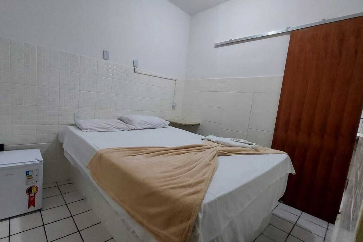 A small, clean room with a bed, a small heater, and a wooden door.