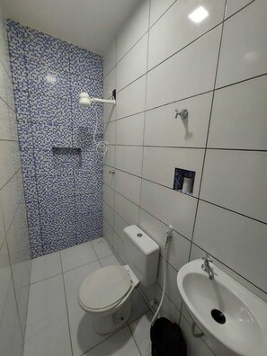 A bathroom with a toilet, bidet, and sink, tiled in white and blue mosaic.