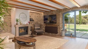 Un salon chaleureux avec une cheminée en pierre, un canapé confortable, une table basse en bois et une grande fenêtre donnant sur l’extérieur.