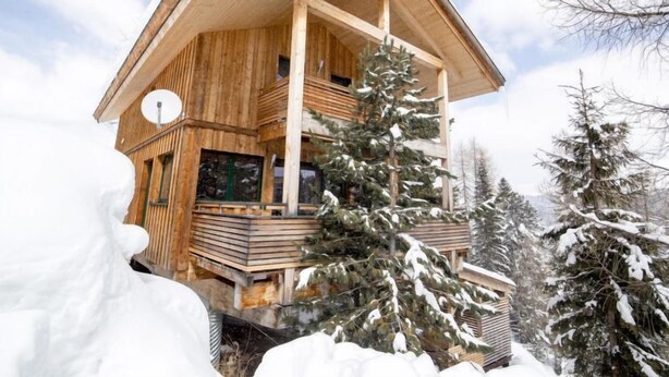 A wooden chalet with a balcony, surrounded by snow-covered trees.