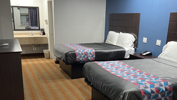 Habitación de hotel con dos camas, un escritorio, baño y espejo.