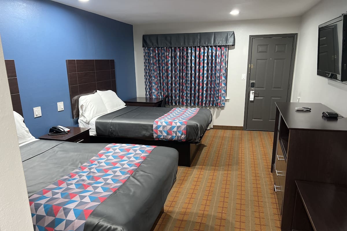 Ein Hotelzimmer mit zwei Betten, einem Schreibtisch, einem Telefon und einer Tür.