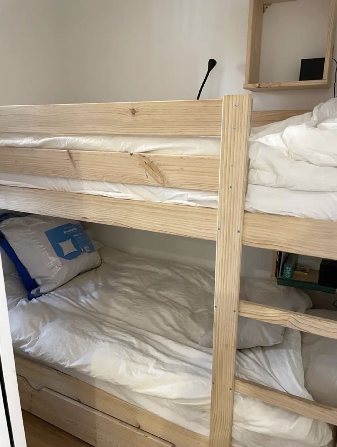 A bunk bed with white bedding and a blue pillow.