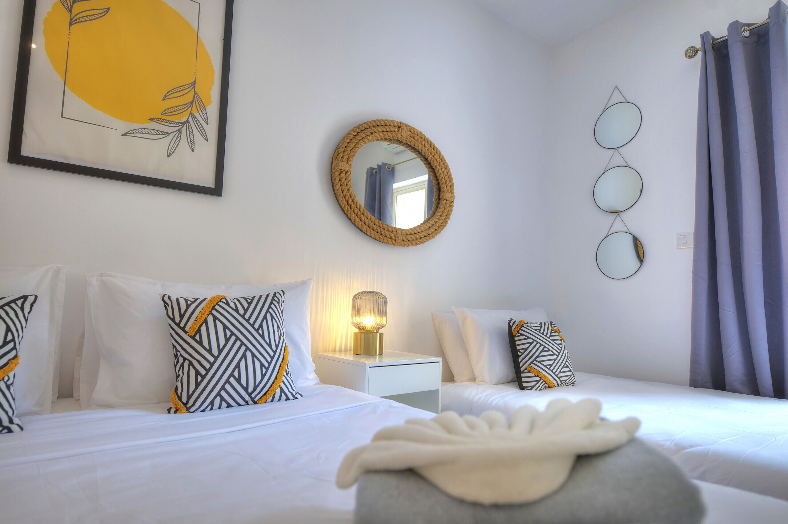 Een hotelkamer met twee bedden, een nachtkastje met een lamp, een spiegel en wanddecoratie.