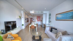 Een moderne woonkamer met een bank, fauteuil en salontafel. Achtergrond toont een eethoek met een tafel en stoelen.