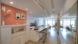Een moderne keuken met witte kasten, een centraal kookeiland met barkrukken en een eetgedeelte met oranje stoelen.