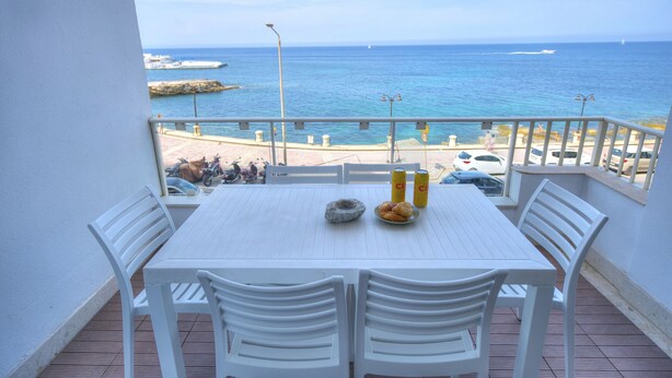 Een balkon met een witte tafel en stoelen, met uitzicht op zee.