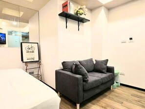 A modern room with a grey sofa, a small black shelf with books and flowers, and a framed inspirational quote.
