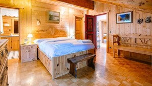 Un dormitorio de cabaña de madera acogedor, con cama, mesita de noche, banco y vistas al exterior.