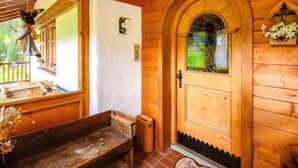 Una cabaña de madera con un banco de madera, una puerta con ventanal y un comedero para pájaros colgante.