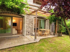 A modern house with a stone exterior, a glass door leading to a living area, and a wooden pergola over a patio. - Luxury House by Interhome (Colico)