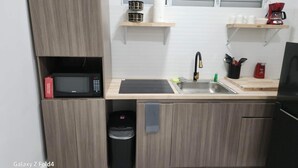 A compact kitchen with a microwave, sink, and storage cabinets. - Scenic Views in Paradise Resorts (Canovanas)